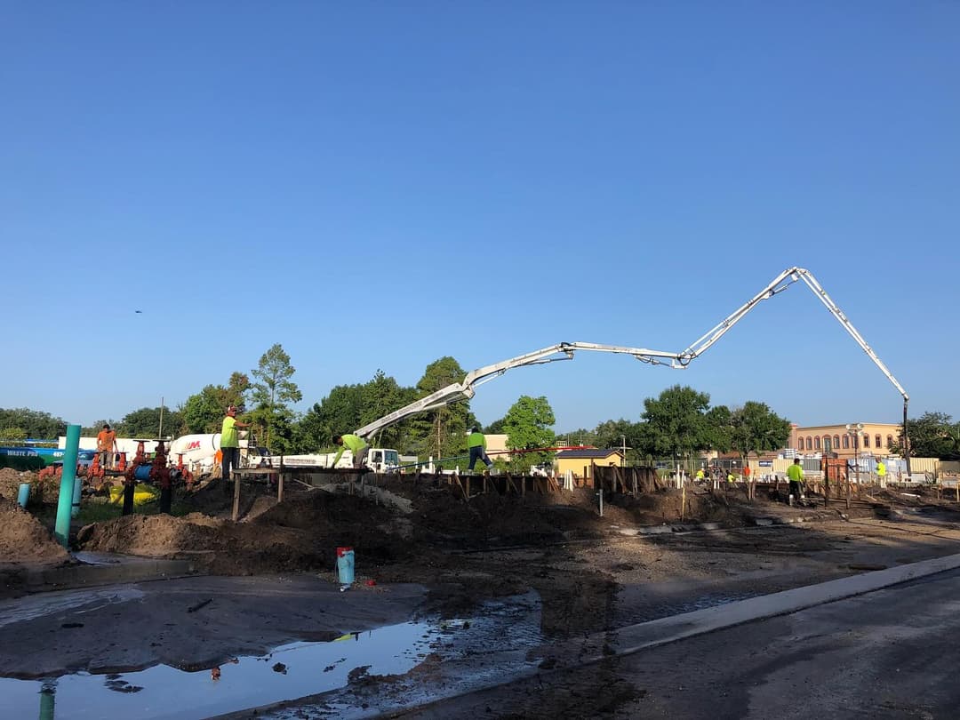 Construction site activity with concrete pump, workers, and machinery under blue sky.
