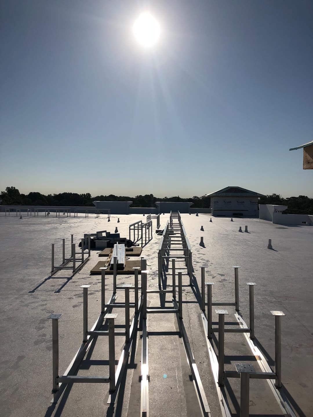 Flat rooftop under bright sun with metal framework ready for installation. Clear blue sky.