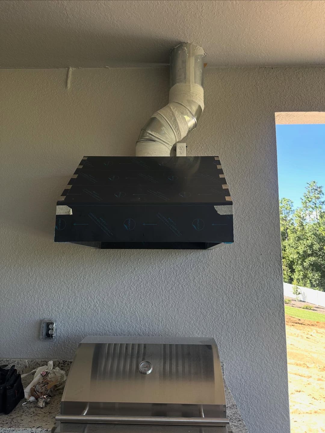 Black kitchen range hood installed above outdoor grill with metal ducting visible.
