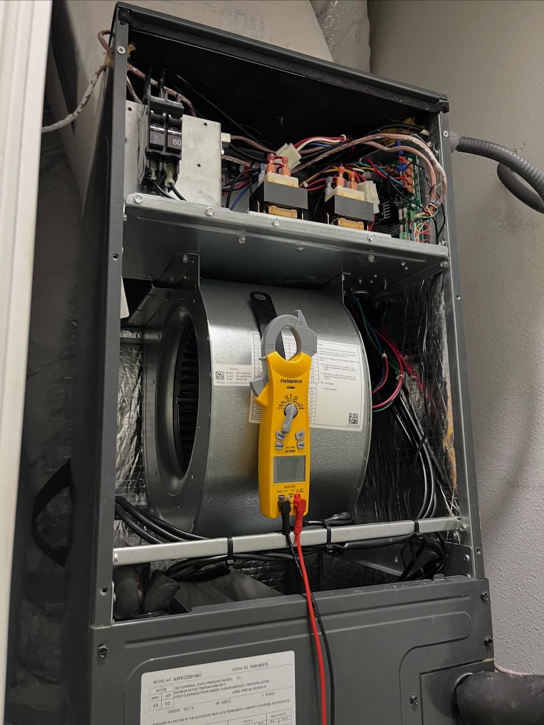 HVAC unit interior with multimeter measuring electrical components and fan motor.