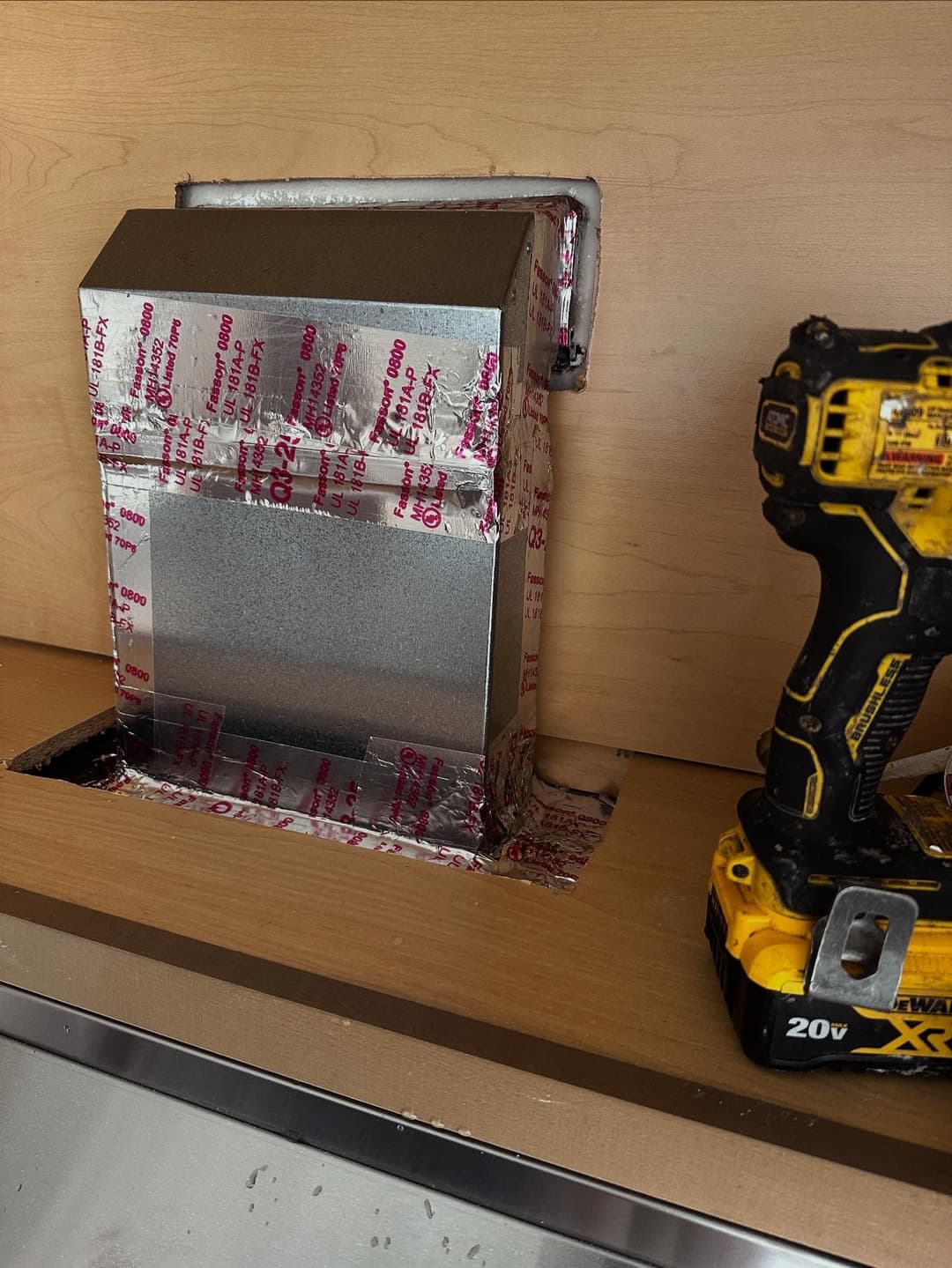Metal vent installation with insulation wrap next to a cordless drill on a countertop.